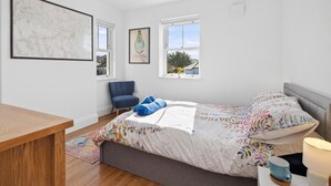 Ein Schlafzimmer mit einem Bett, einem Sessel, einem Tisch und zwei Fenstern.