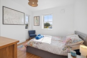 Un dormitorio con una cama, una silla, una mesa y dos ventanas.