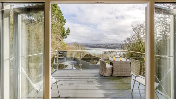 A balcony with a view of a cityscape, a table with chairs, and a glass railing.