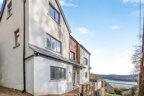A two-story house with a stone foundation, large windows, and a view of a body of water.