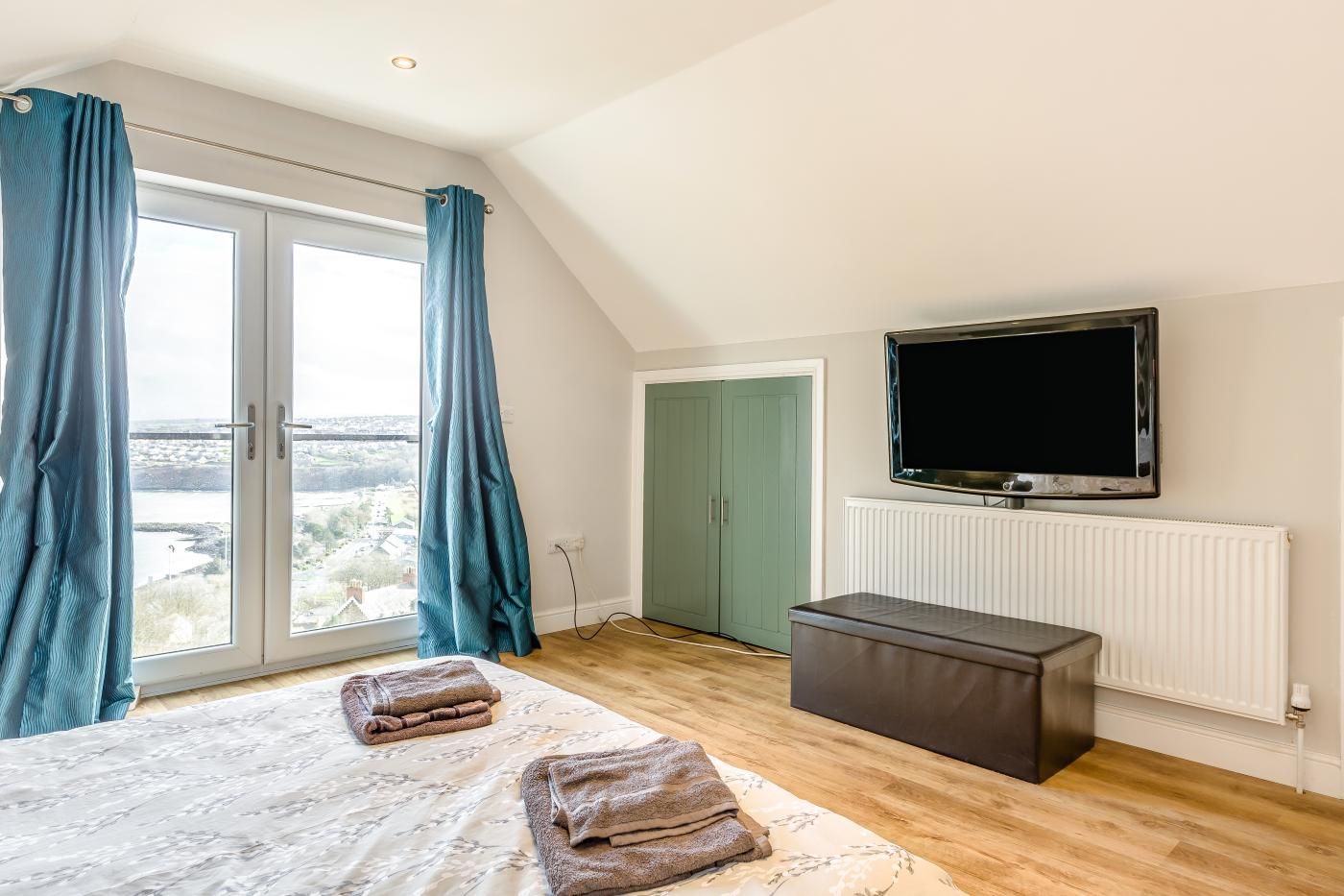 A bedroom with a bed, a TV, a wardrobe, and a view through a large window.