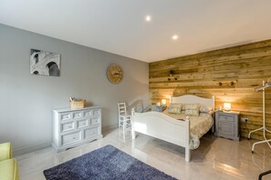 A bedroom with a bed, nightstands, a dresser, a chair, a clock, and a wall-mounted shelf.