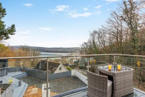 A balcony with a glass railing overlooking a body of water and a distant town.