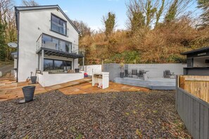 A modern two-story house with a patio area, a barbecue setup, and a wooden fence.
