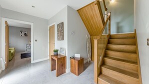A modern interior with a wooden staircase, a reception desk, and a hallway leading to a living area.