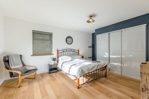 A bedroom with a bed, a chair, a bedside table, a mirror, and a sliding glass door. - 4 Bed in Goodwick (oc-s34887) (Goodwick)