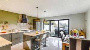 A modern kitchen with a central island, a dining area with a table and chairs, and a large sliding glass door leading to an outdoor space.