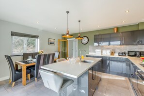 A modern kitchen with a central island, a dining area with chairs, and a large window.