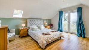 A bedroom with a large bed, a desk, a chair, a window with curtains, and a skylight.