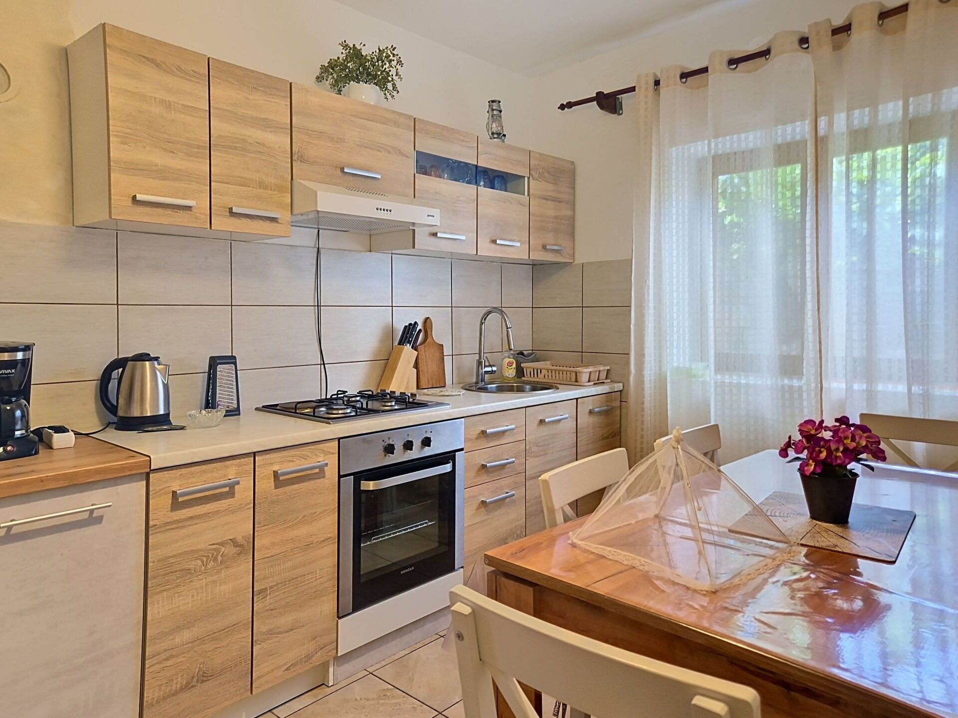 A modern kitchen with wooden cabinets, a gas stove, an oven, and a dining area with a table and chairs.