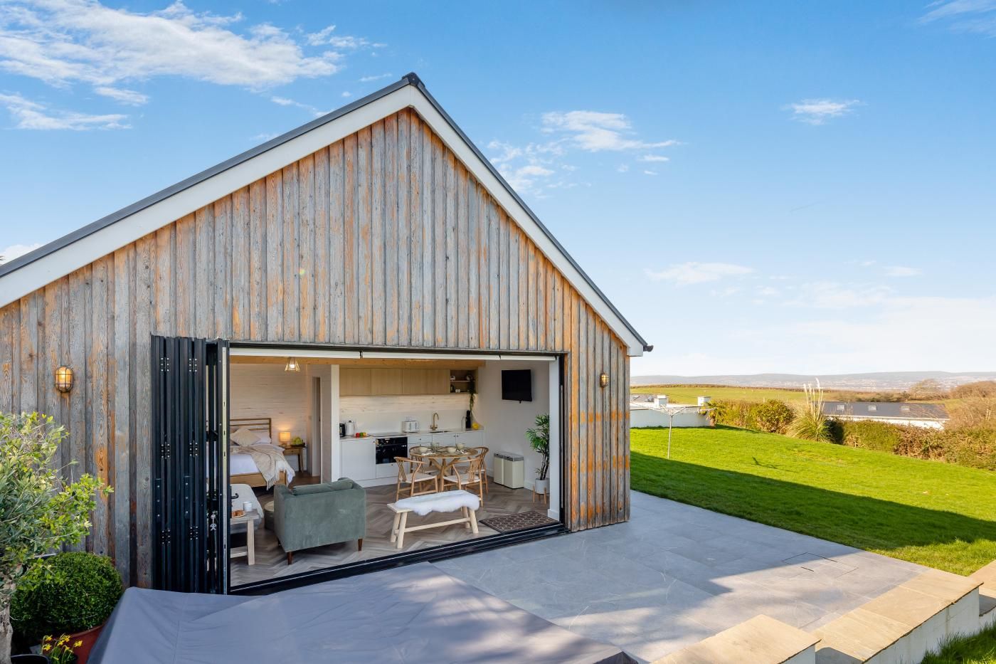 Un bâtiment moderne de style grange, avec une cuisine et un coin repas visibles à travers une porte ouverte.
