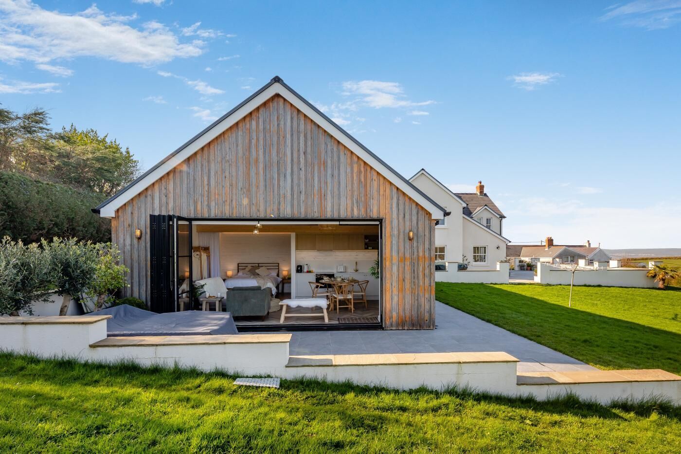 A modern house with a large open garage, a dining area, and a well-maintained lawn.