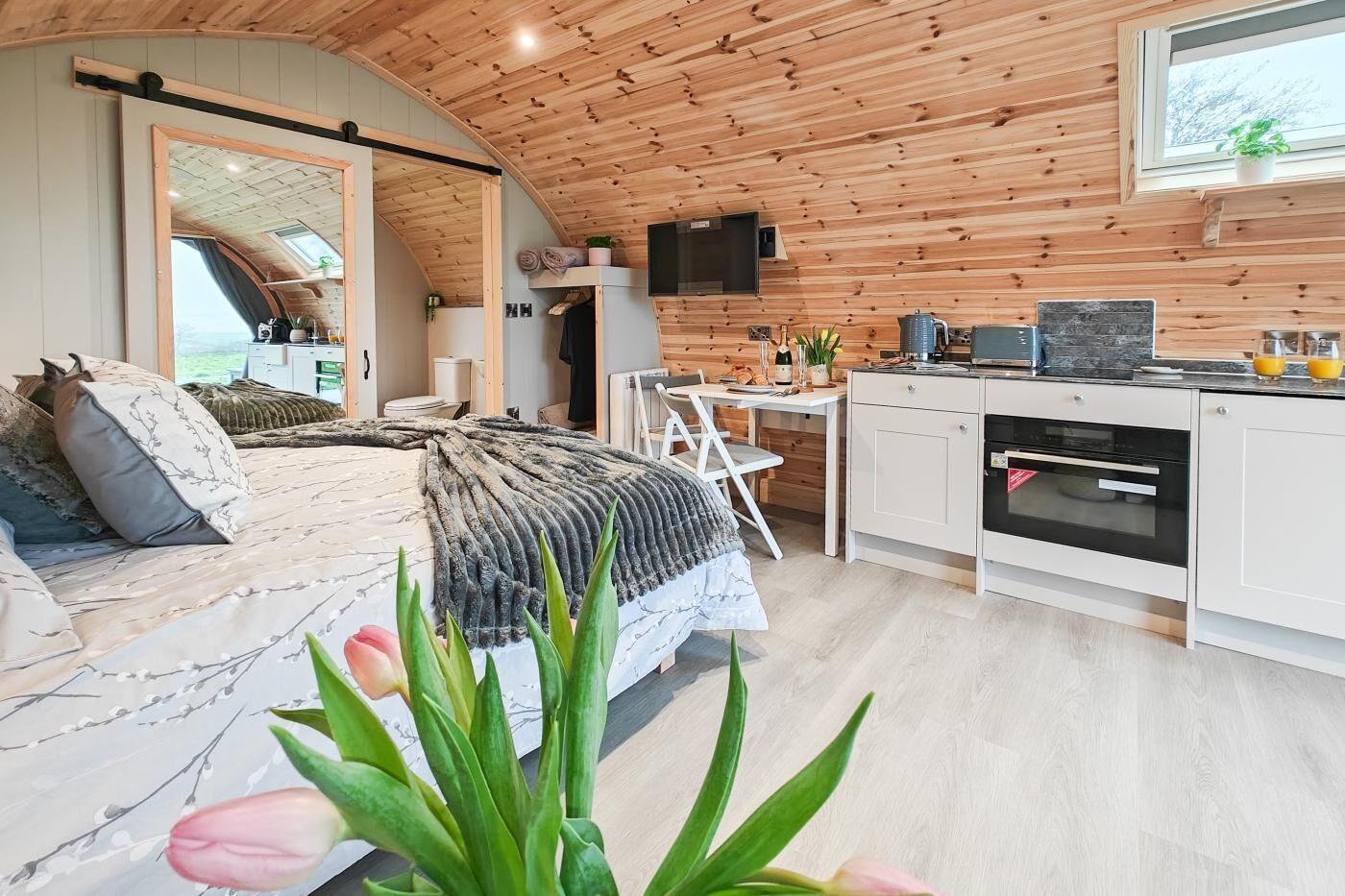 A bedroom with a bed, a desk, and a kitchenette.