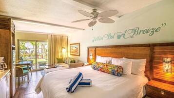 A hotel room with a bed, a ceiling fan, a wall with a quote, a dining area with a table and chairs, and a view through the glass doors.