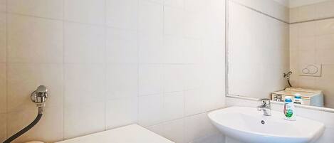A bathroom with white tiles, a sink, a mirror, and a towel dispenser.