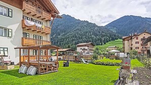 Ein mehrstöckiges Gebäude mit Balkonen, einer überdachten Außenbestuhlung und Blick auf eine gebirgige Landschaft.