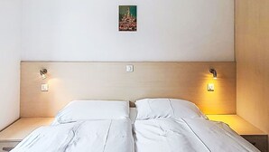 Ein Doppelbett mit weißen Laken, zwei Nachttische, eine Wandleuchte und ein kleines gerahmtes Bild an der Wand.