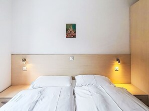 Ein Doppelbett mit weißen Laken, zwei Nachttische, eine Wandleuchte und ein kleines gerahmtes Bild an der Wand.