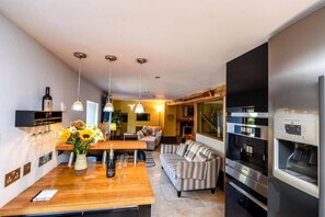A modern kitchen with a wooden countertop, wine bottle, and glasses, a striped sofa, and a built-in oven. - 5 Bed in Tuckenhay (oc-o35004) (Tuckenhay)