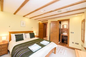 A bedroom with a bed, wooden headboard, bedside tables, a bathroom with a sink and mirror, and a door leading to another room. - 5 Bed in Tuckenhay (oc-o35004) (Tuckenhay)