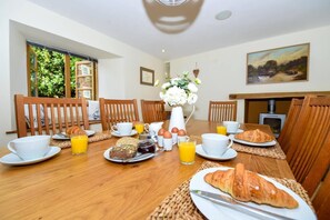A breakfast setting with a wooden table, chairs, breakfast items, and a painting on the wall. - 5 Bed in Tuckenhay (oc-o35004) (Tuckenhay)