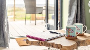 Een houten tafel met een notitieboek, pen en twee mokken met uilenprint op een balkon met uitzicht.