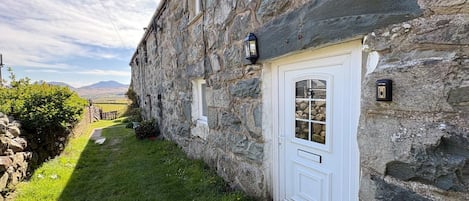 Un edificio de piedra con una puerta blanca, un ventanal pequeño y un buzón.
