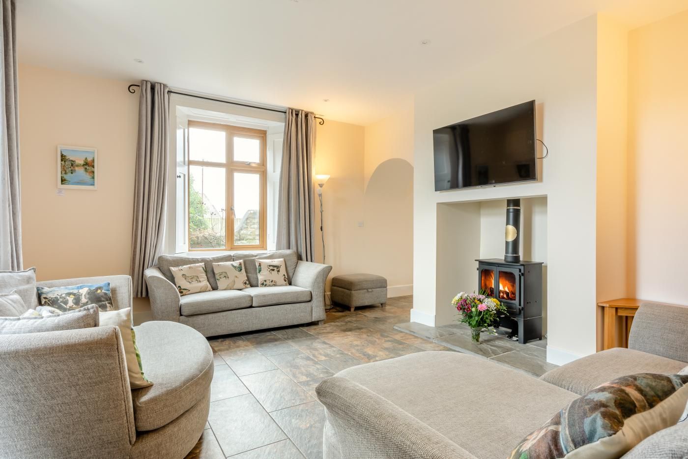 Una sala de estar con sofá, sillones, chimenea, televisor y ventana con cortinas.