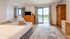 A bedroom with a bed, a TV, a wooden dresser, a wardrobe, and a balcony with curtains. - 3 Bed in West Pennard (oc-b34974) (Coxbridge)