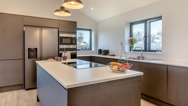 A modern kitchen with a central island, stainless steel appliances, pendant lighting, and a view through the window. - 3 Bed in West Pennard (oc-b34974) (Coxbridge)