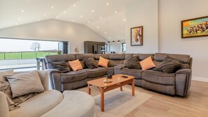 A modern living room with a sectional sofa, a round ottoman, and a wooden coffee table. - 3 Bed in West Pennard (oc-b34974) (Coxbridge)