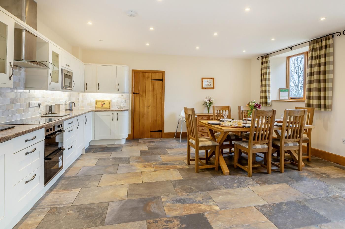 A modern kitchen with white cabinetry, a central island, and a dining area with wooden chairs and a table.
