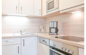 A modern kitchen with white cabinetry, a built-in microwave, a coffee maker, and a dishwasher. - Ferienwohnung mit Badewanne in Sellin (Sellin)