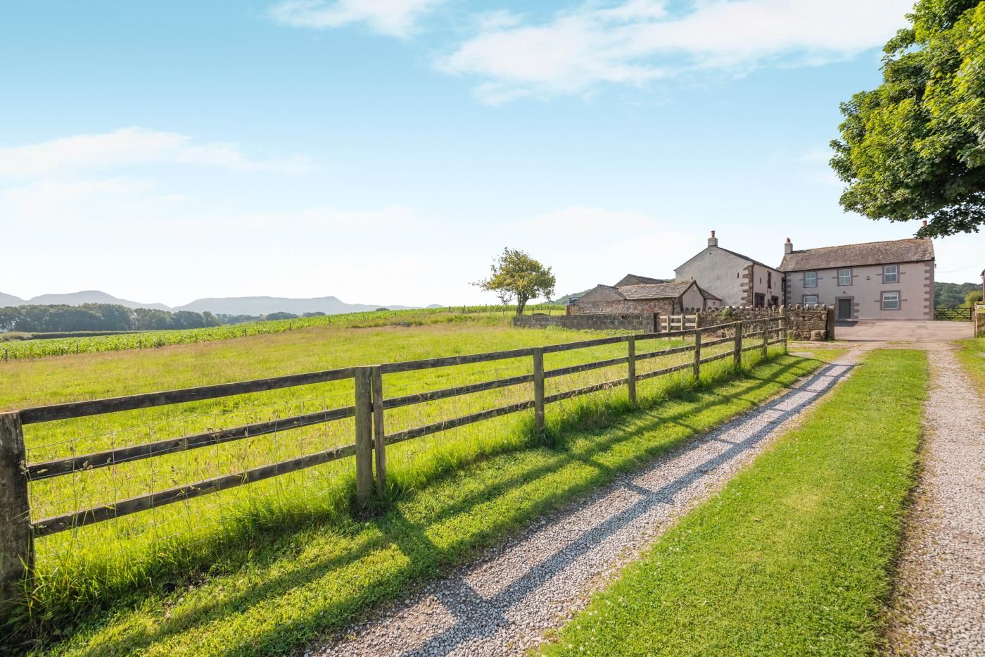 A rural property with a gravel path, wooden fence, and a building with a stone wall.