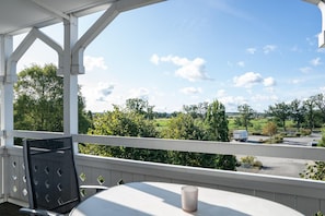 A balcony with a table and chair, overlooking a parking area and greenery. - Ferienwohnung in Sellin mit Balkon, Hund (Sellin)