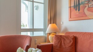 A room with a sofa, a lamp, a window, and a painting on the wall. - Ferienwohnung in Sellin mit Balkon, Hund (Sellin)