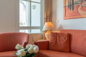 A room with a sofa, a lamp, a window, and a painting on the wall. - Ferienwohnung in Sellin mit Balkon, Hund (Sellin)