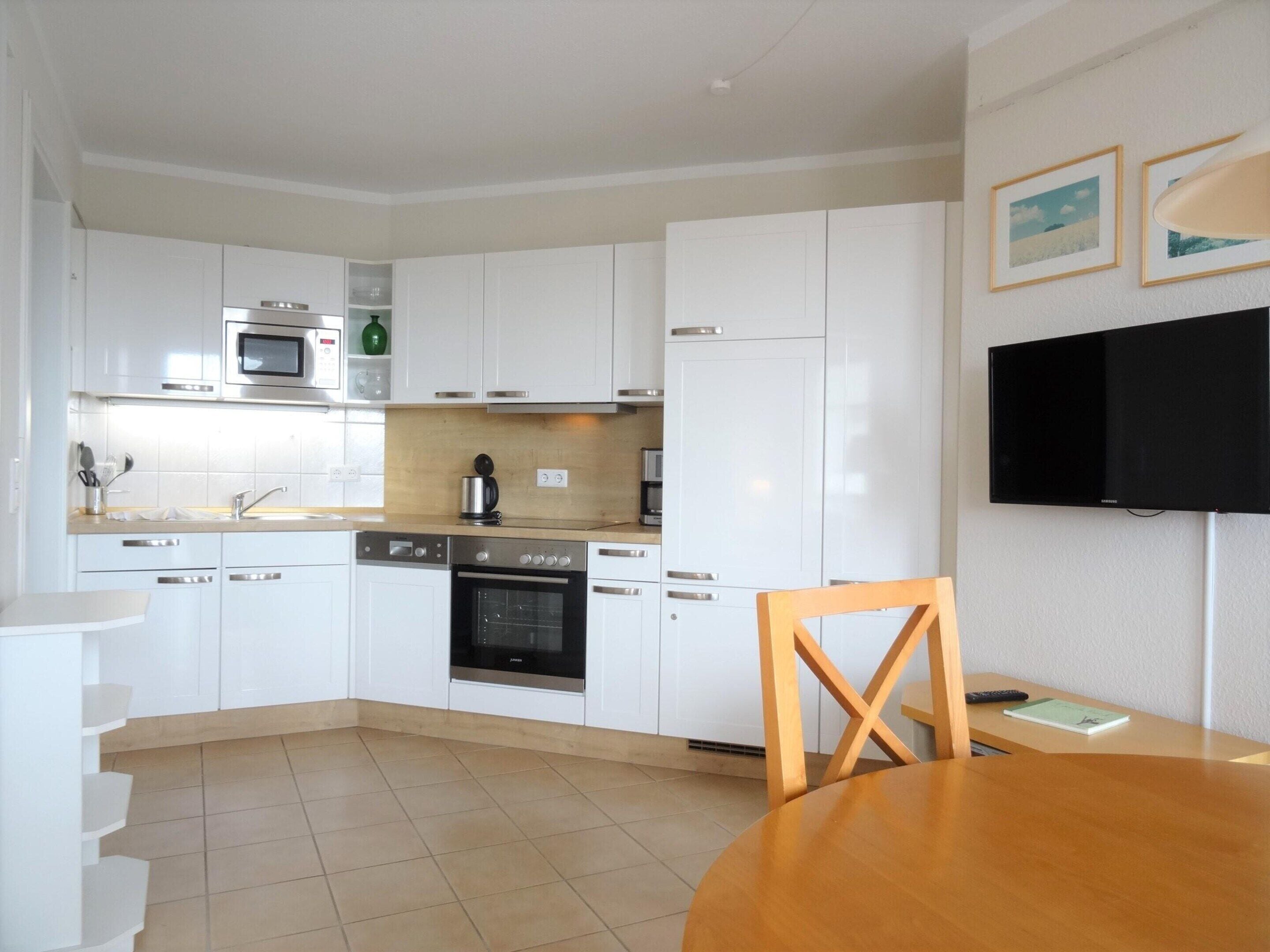 A compact kitchen with white cabinets, a microwave, a coffee maker, and a TV mounted on the wall.