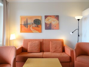 Un salon avec un canapé, deux coussins, une table basse et deux tableaux accrochés au mur.
