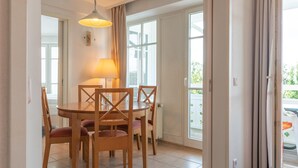 A dining area with a round table, four chairs, a lamp, and a view through a glass door. - Ferienwohnung in Sellin mit Balkon, Hund (Sellin)