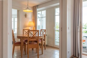 A dining area with a round table, four chairs, a lamp, and a view through a glass door. - Ferienwohnung in Sellin mit Balkon, Hund (Sellin)