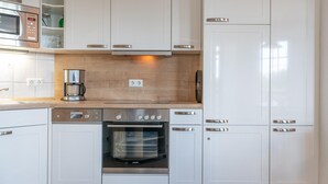 A modern kitchen with white cabinetry, a Bosch dishwasher, a built-in oven, and a coffee maker. - Ferienwohnung in Sellin mit Balkon, Hund (Sellin)