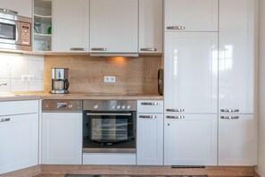 A modern kitchen with white cabinetry, a Bosch dishwasher, a built-in oven, and a coffee maker. - Ferienwohnung in Sellin mit Balkon, Hund (Sellin)