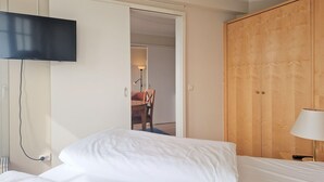A hotel room with a bed, a TV mounted on the wall, a wooden wardrobe, and a lamp. - Ferienwohnung in Sellin mit Balkon, Hund (Sellin)