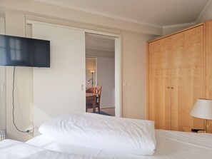 A hotel room with a bed, a TV mounted on the wall, a wooden wardrobe, and a lamp. - Ferienwohnung in Sellin mit Balkon, Hund (Sellin)