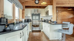 A kitchen with white cabinets, a central stove, and a bar area with a high chair. - 3 Bed in Ravensworth (oc-s34987) (Ravensworth)