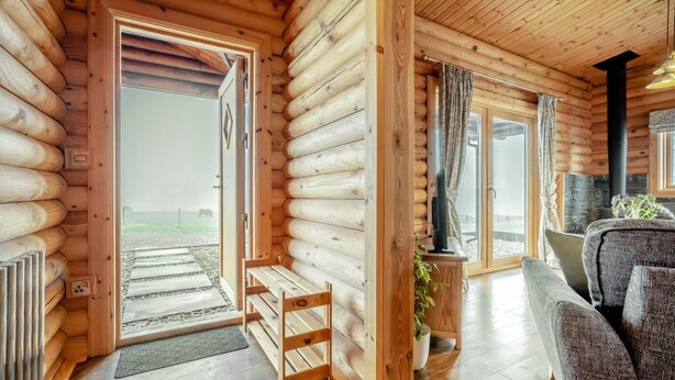 A log cabin interior with a wooden bench, a sofa, a television, and a large window. - 3 Bed in Ravensworth (oc-s34987) (Ravensworth)