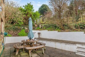 An outdoor patio with a round table, benches, and a green umbrella. - 3 Bed in Polruan (oc-l35010) (Fowey)