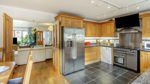 A modern kitchen with stainless steel appliances, wooden cabinets, and a dining area with a table and chairs. - 3 Bed in Polruan (oc-l35010) (Fowey)