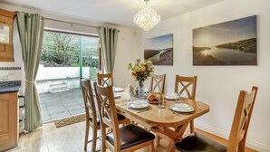 A dining area with a table set for four, wooden chairs, a chandelier, and two landscape paintings on the wall. - 3 Bed in Polruan (oc-l35010) (Fowey)